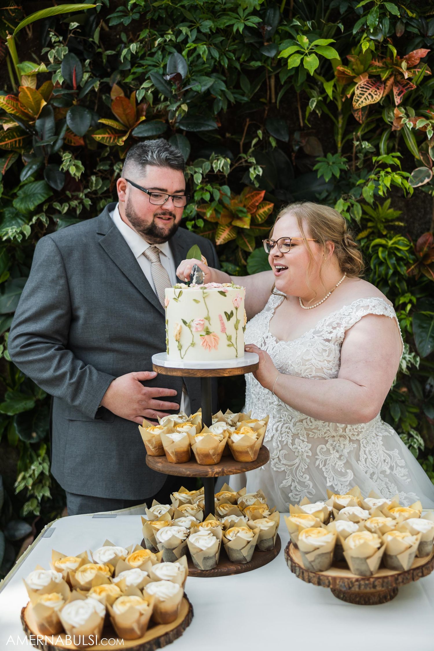 Wedding couple admiring their tiered cake and cupcake display at outdoor reception.