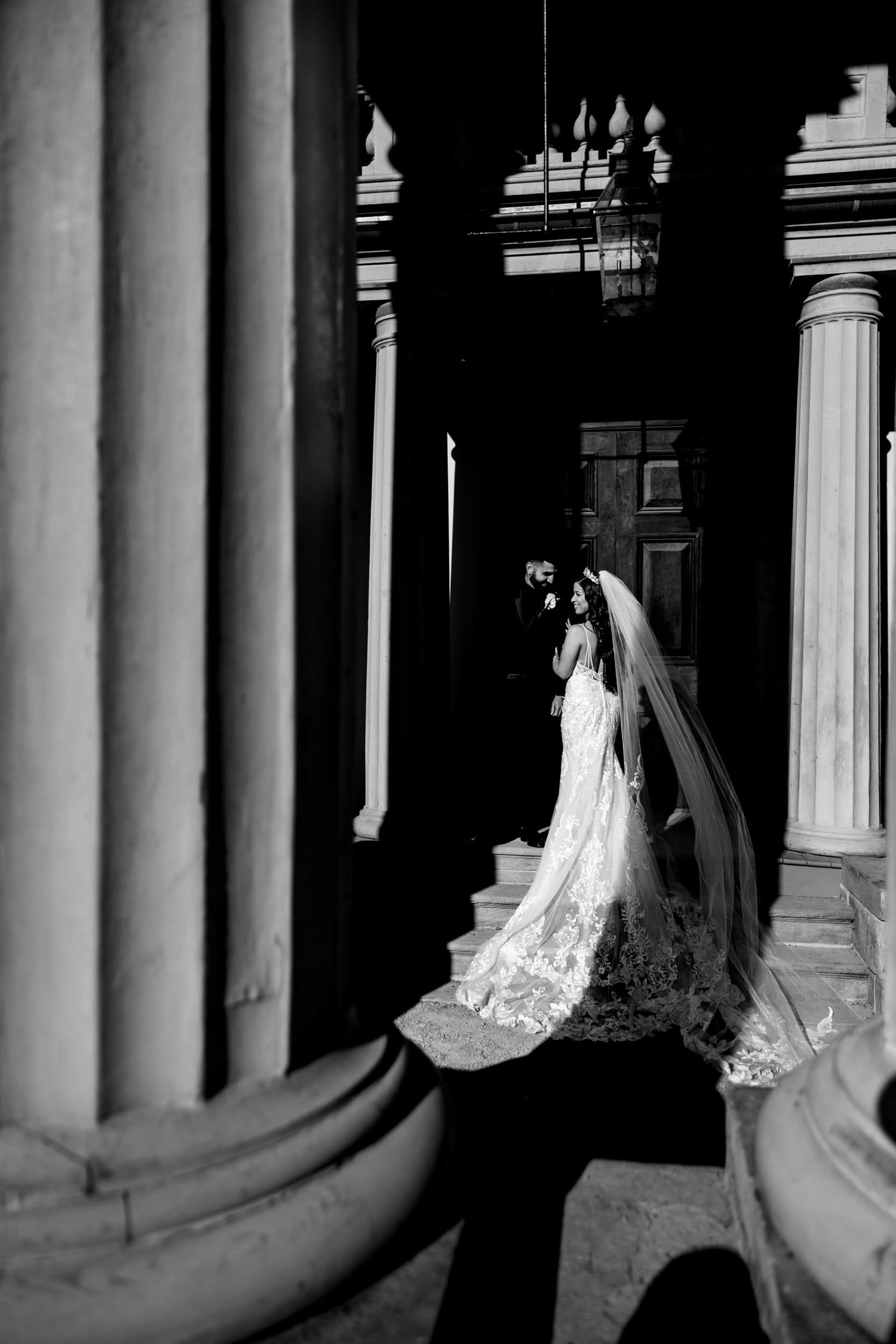 Black and white architectural wedding photo featuring classical columns and dramatic lighting.