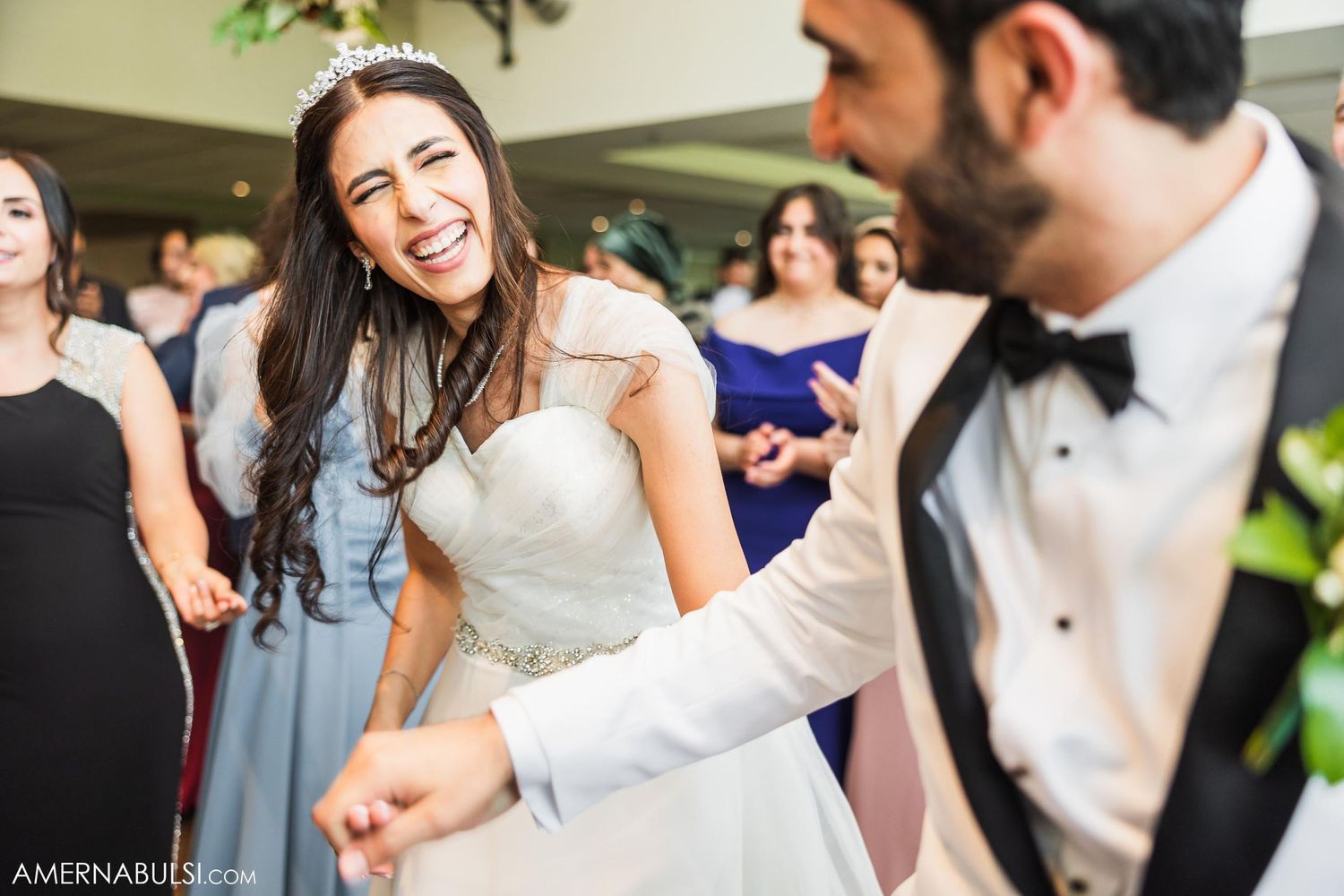 Joyful dancing and celebration during wedding reception with guests in background.
