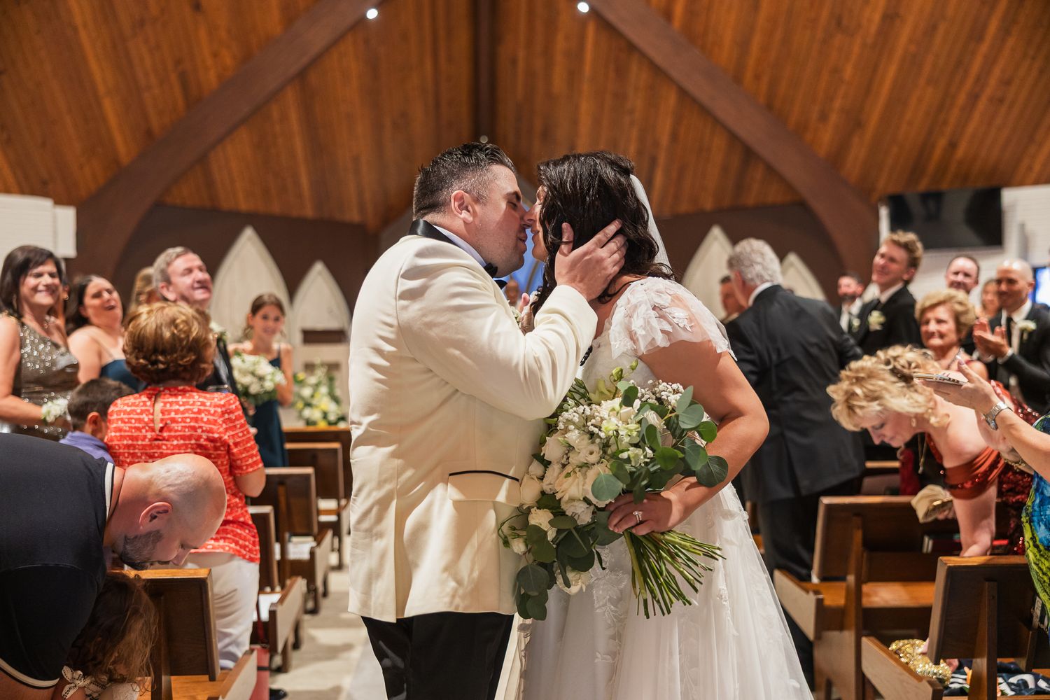 Bride and groom share their first kiss at the altar during their wedding ceremony in a wooden church.