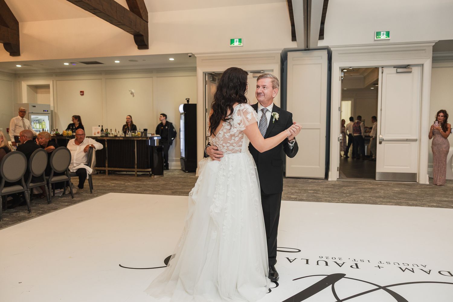 Bride and groom share their first dance on a white dance floor at an elegant wedding reception venue.