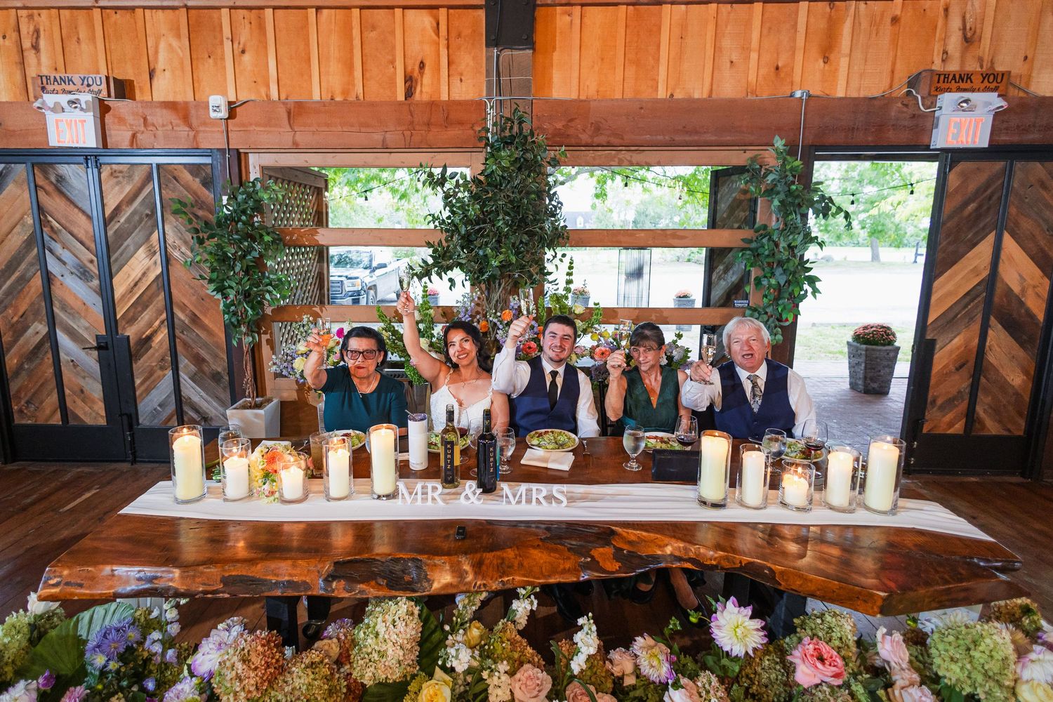 Wedding party raising glasses in a toast at a decorated head table with Mr. and Mrs. sign.