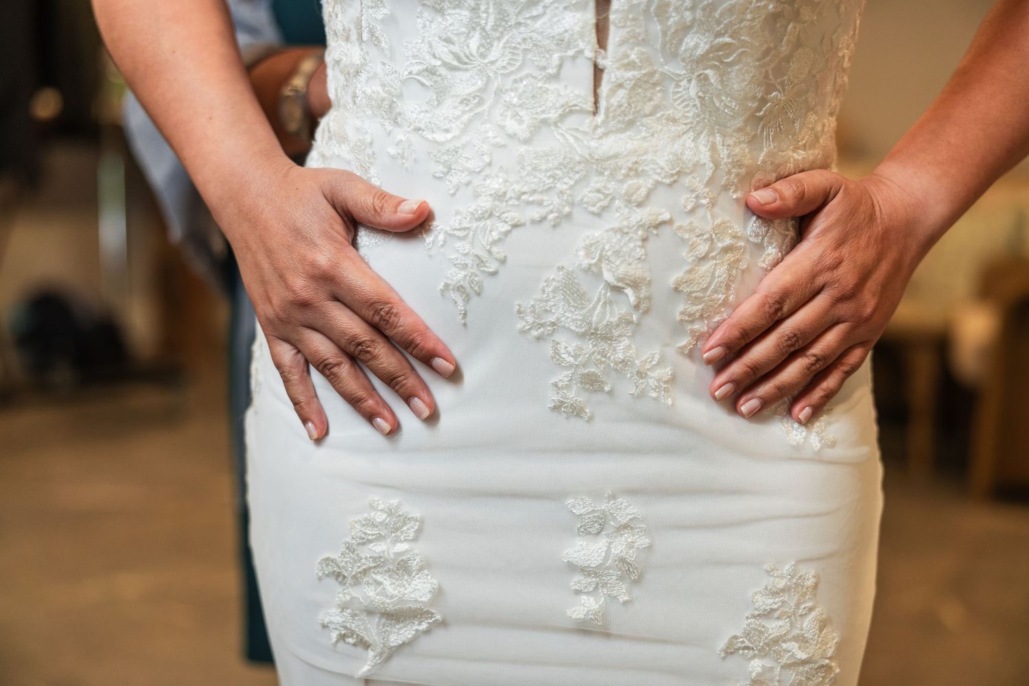 Close-up of a bride in a white lace wedding dress with hands gently placed on her waist.