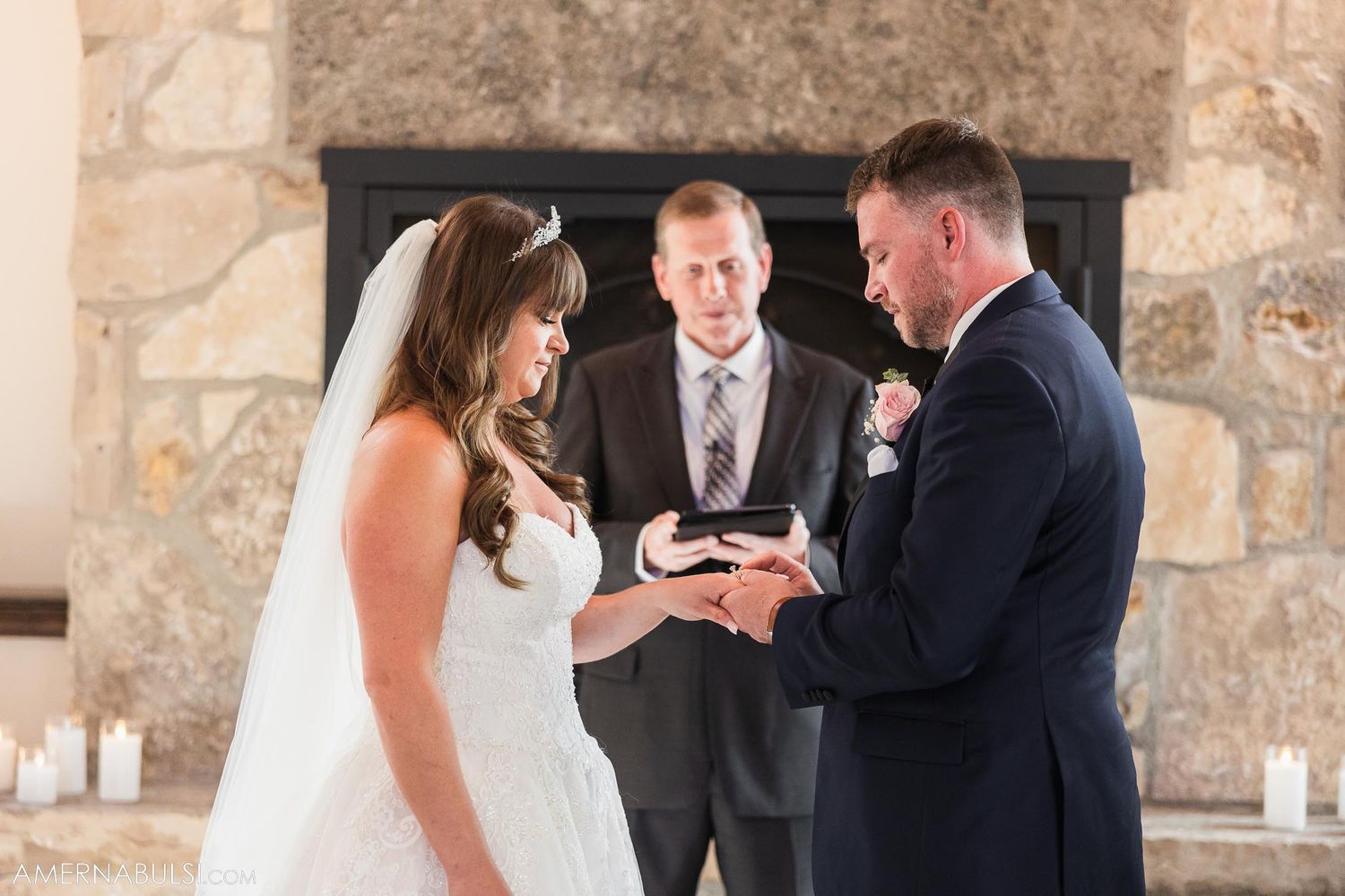 Wedding ceremony with stone fireplace backdrop as couple exchanges rings.