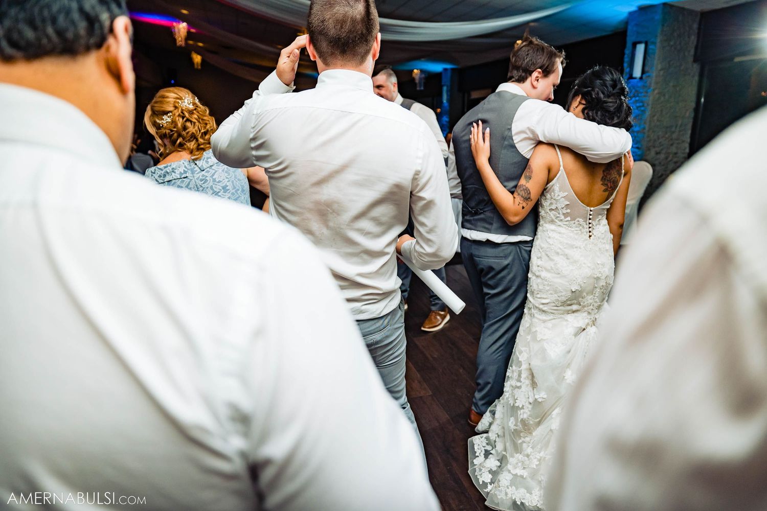 Wedding guests slow dancing in close embrace on dance floor during reception.