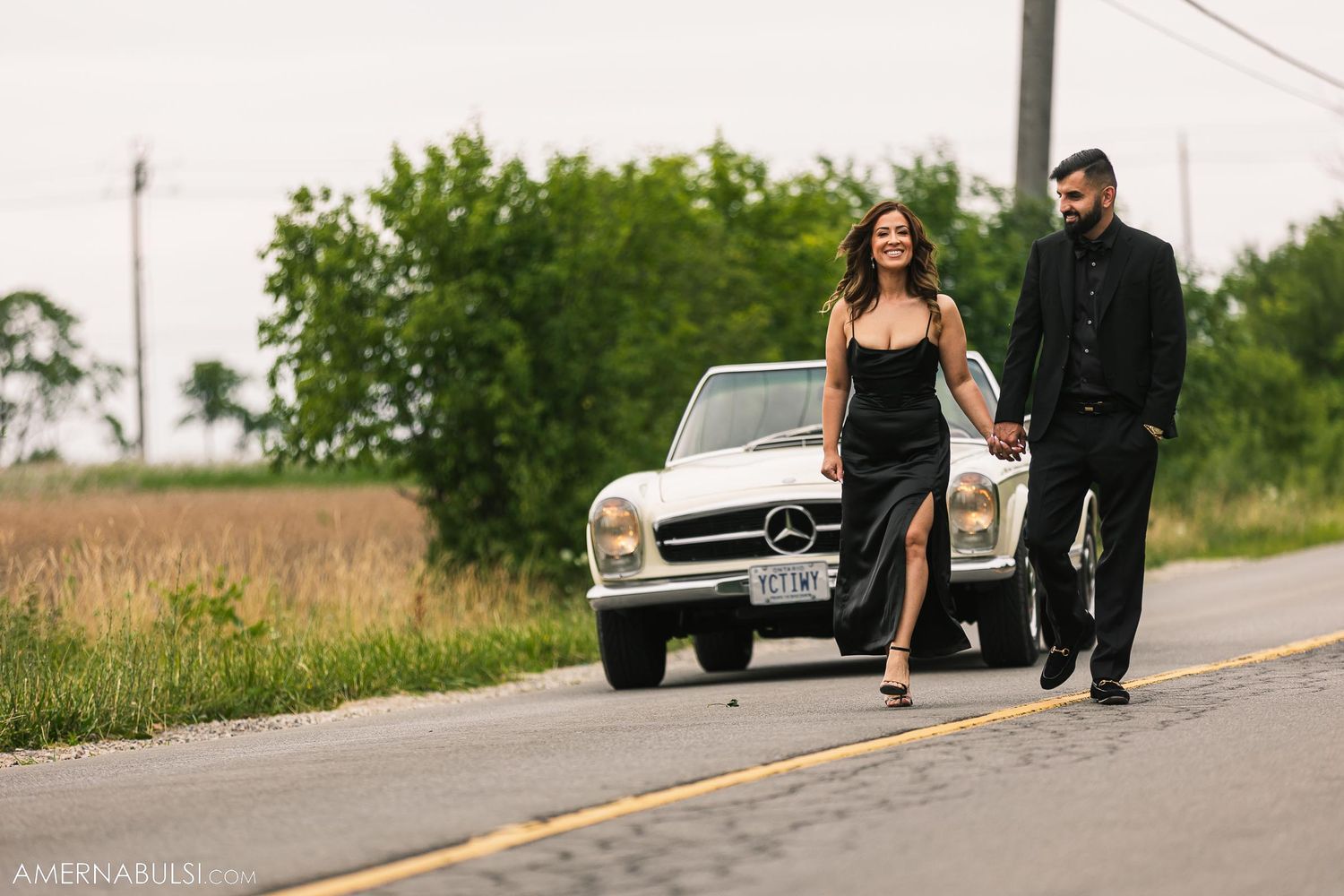 Couple in formal black attire walking alongside vintage Mercedes-Benz.