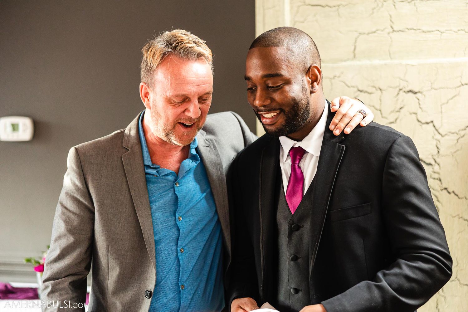 Two people sharing a laugh and embracing at a formal event.