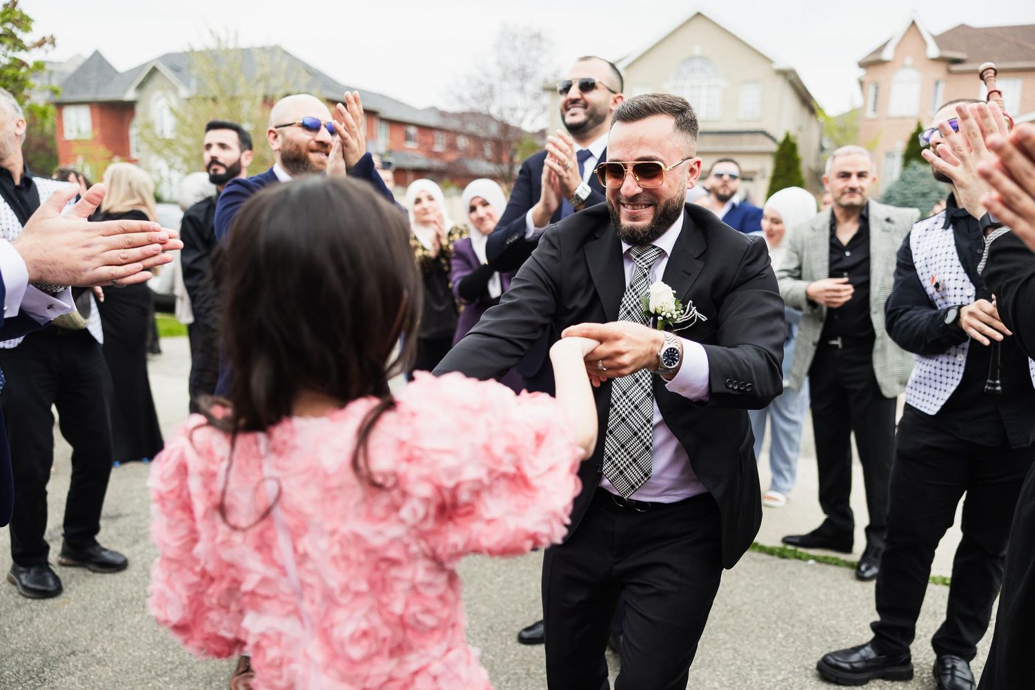 Wedding guests celebrate with dancing and laughter in a suburban street.