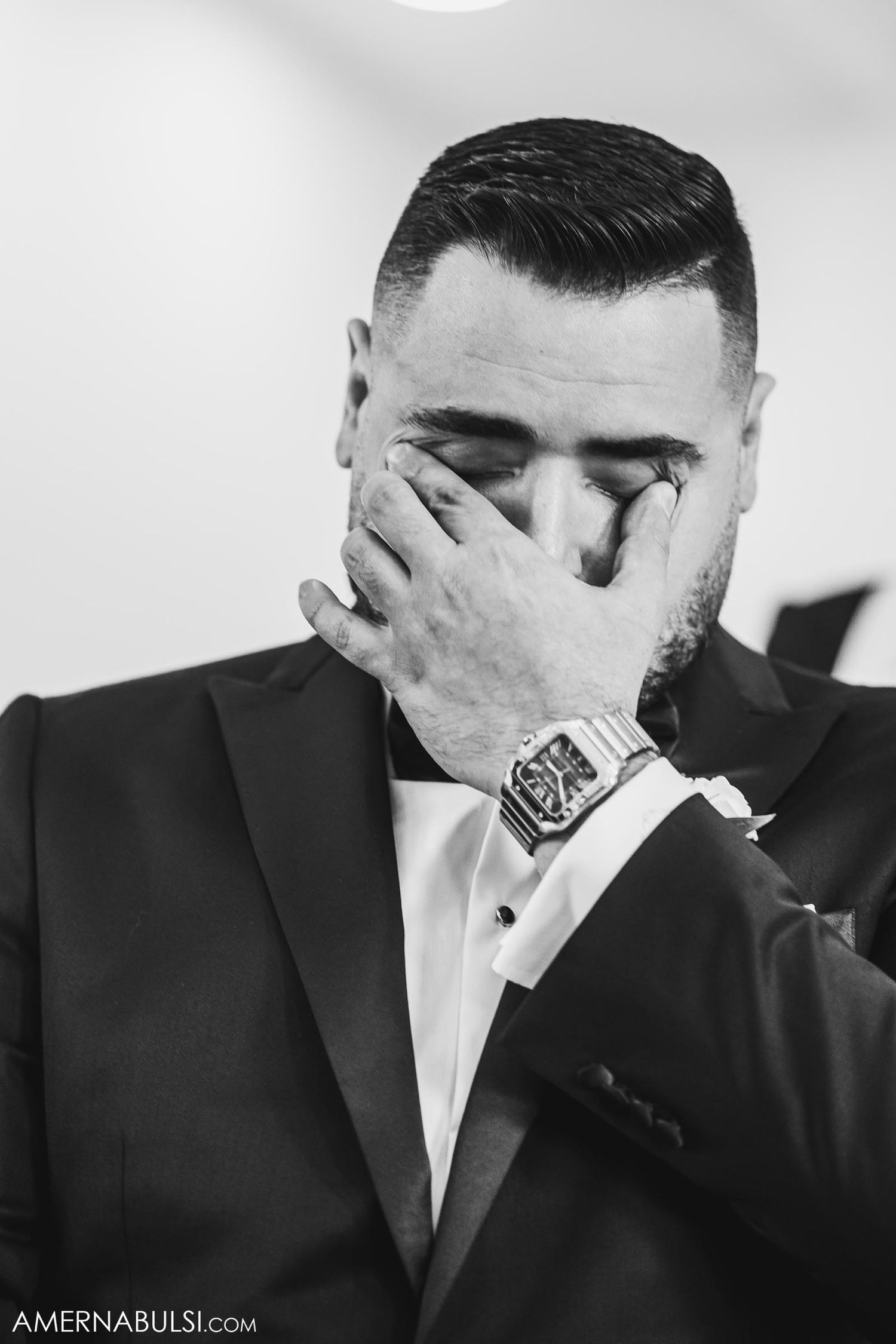 Black and white portrait of an emotional groom covering his face during a wedding ceremony.
