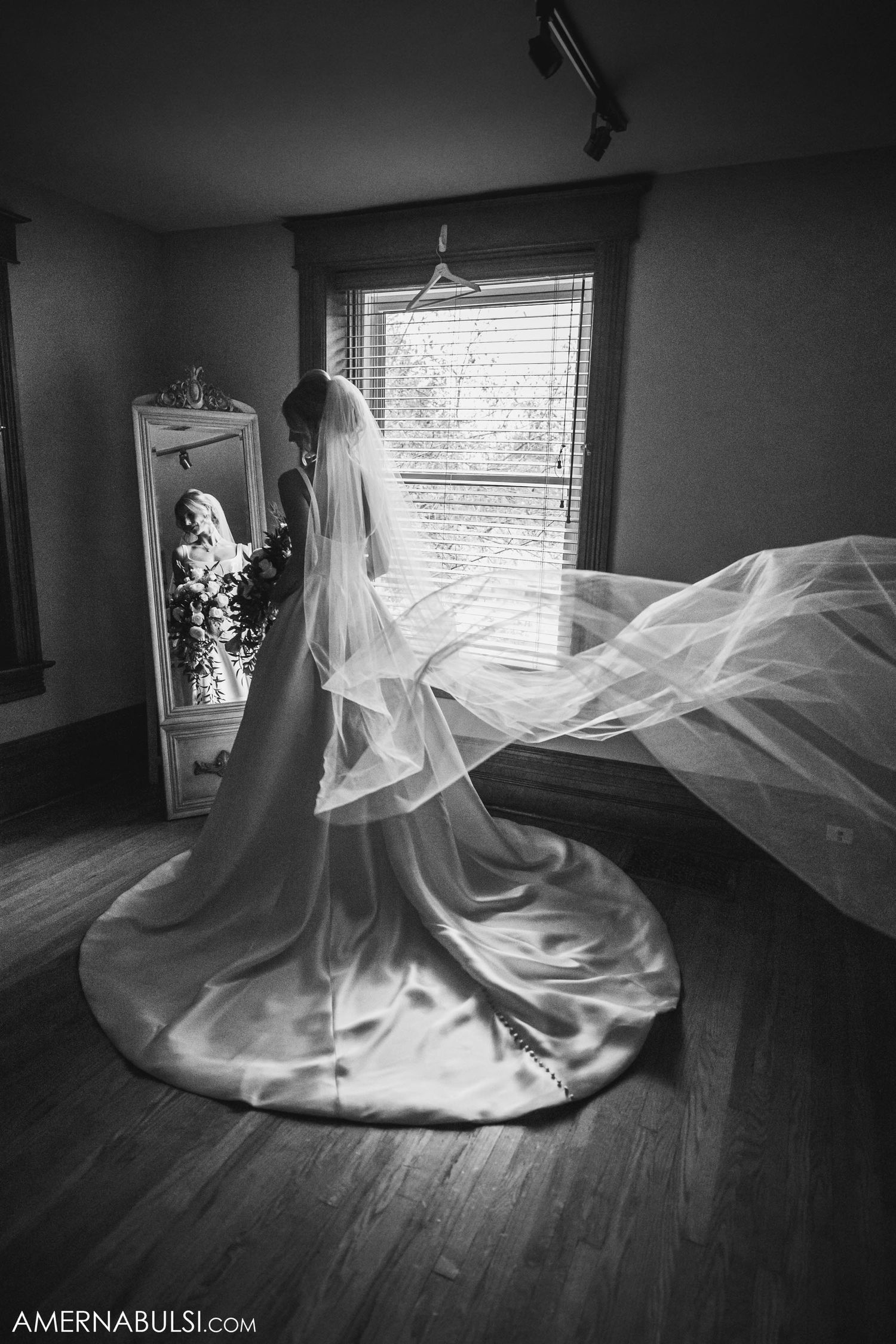 A flowing wedding veil catches the light as it billows dramatically in a black and white photo.