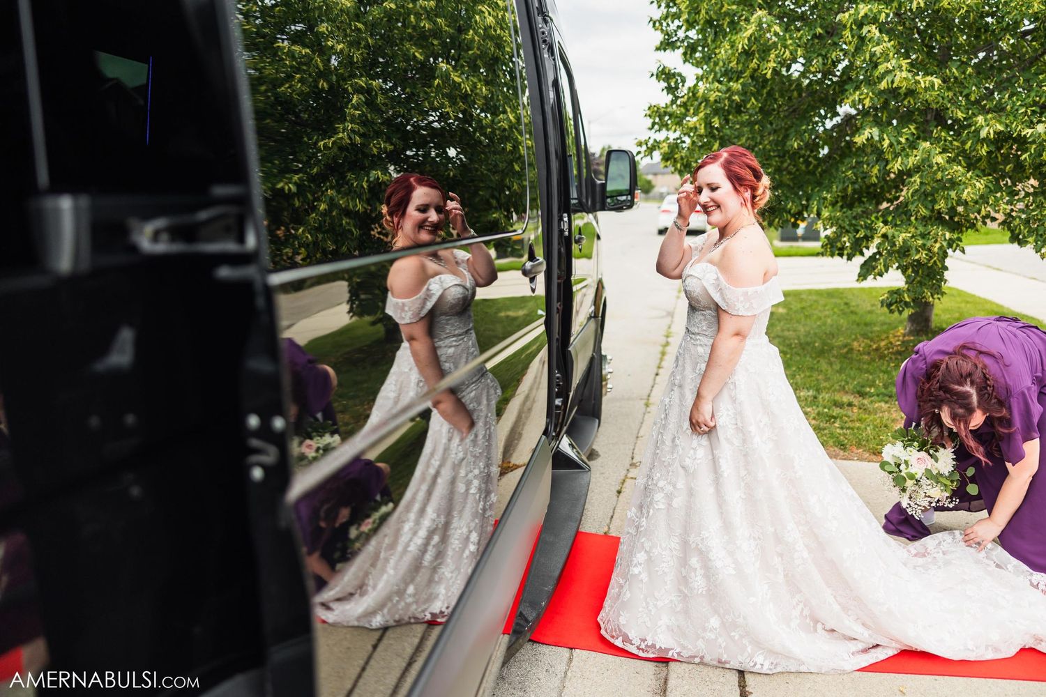 Two brides in white wedding dresses smile and laugh while standing next to a vehicle outdoors.