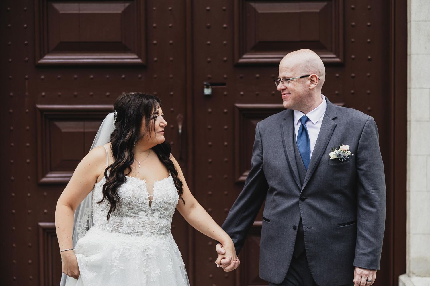 Candid moment of newlyweds standing in front of large wooden doors.