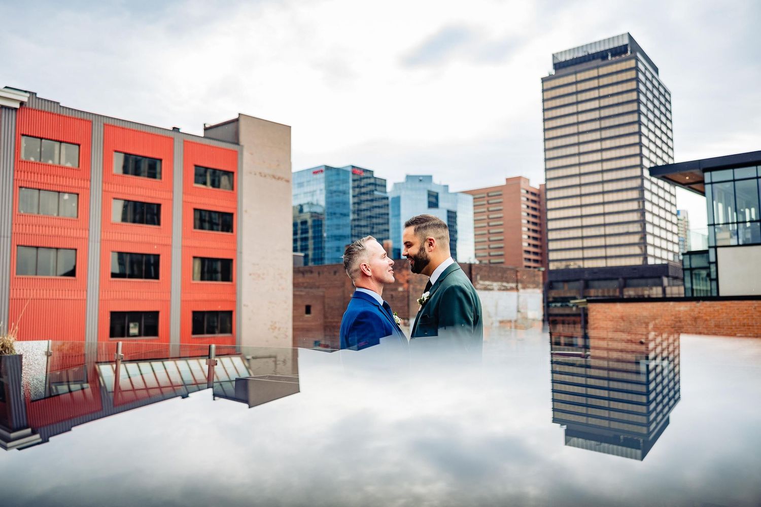 Urban wedding photo with cityscape reflections in puddle creating mirror effect.