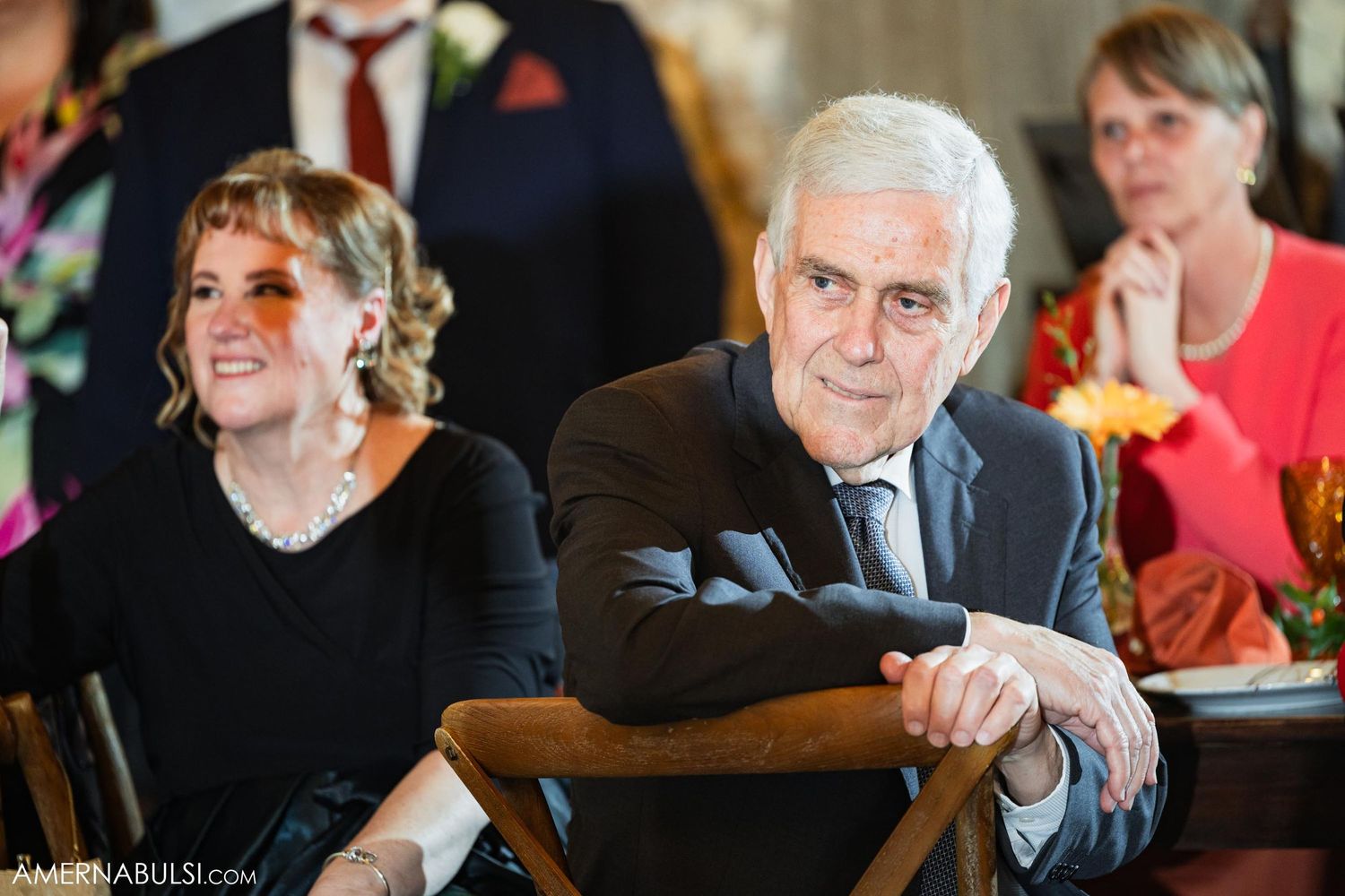 Wedding guests smile and react during reception speeches in a rustic venue.