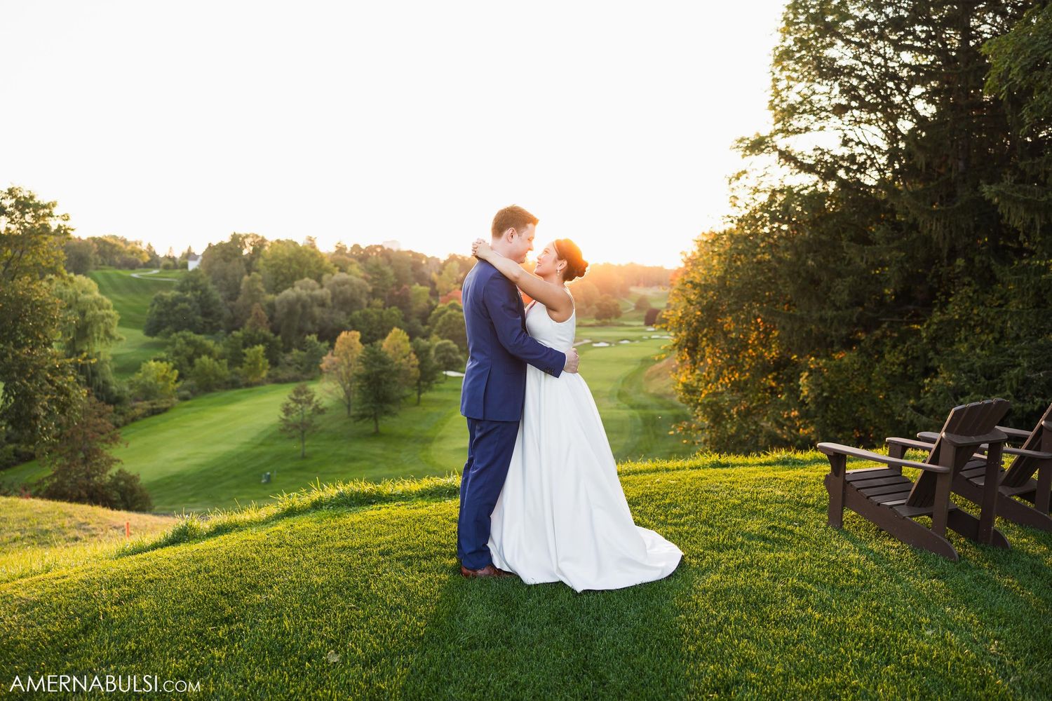 Newlyweds embrace on a scenic hilltop overlooking rolling green hills at sunset.