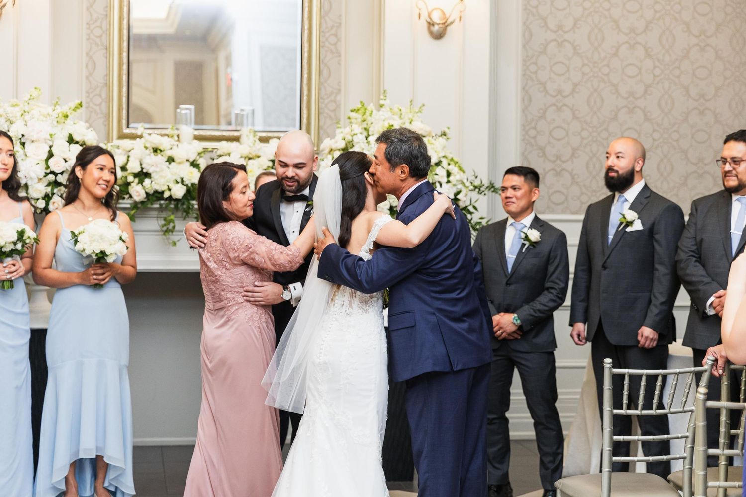 Emotional wedding ceremony moment unfolds with wedding party and floral decorations in elegant venue.