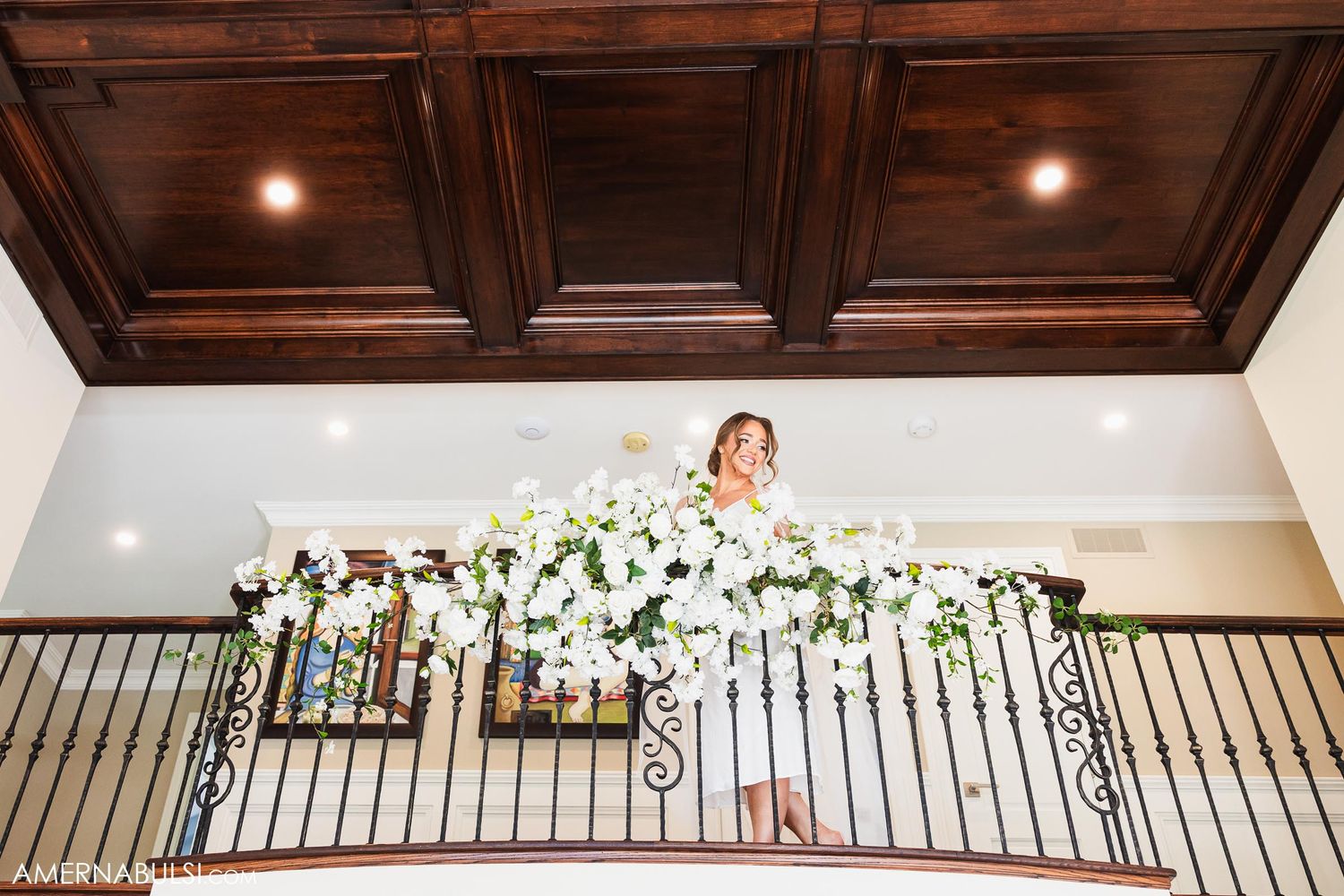 White floral garlands decorate an ornate balcony railing beneath a dark wood coffered ceiling.