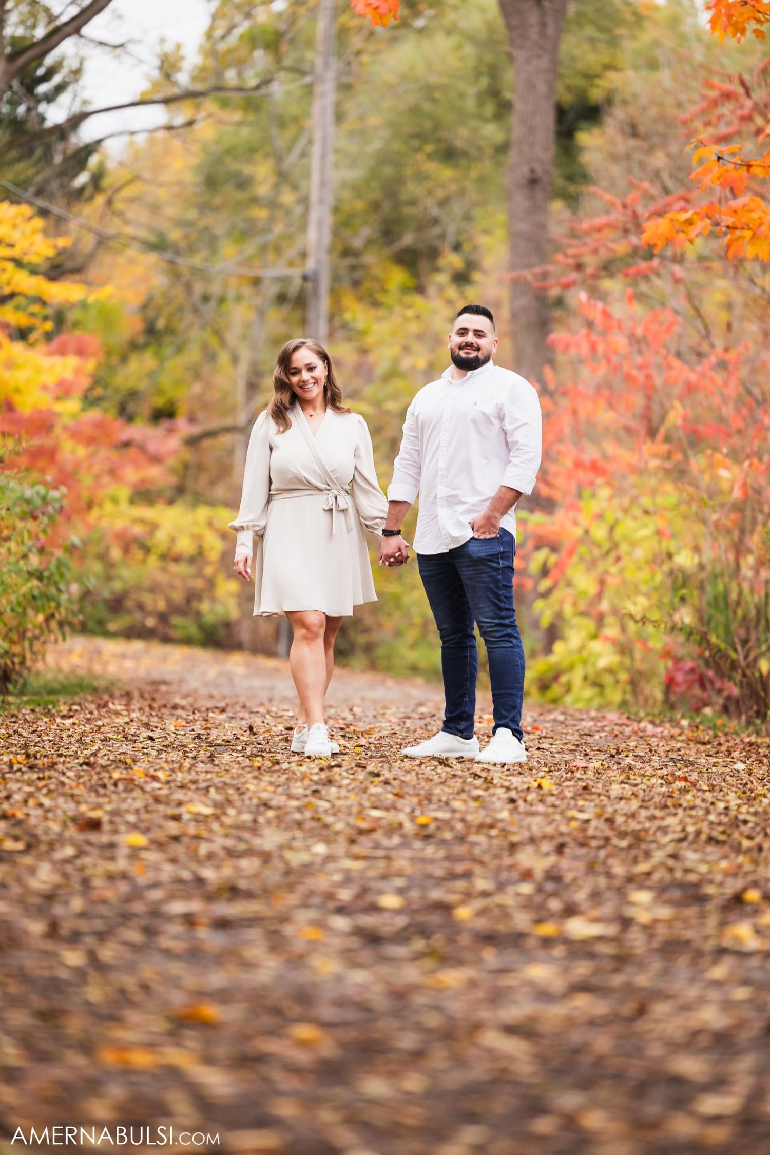 A couple walks hand in hand down a leaf-covered path surrounded by autumn colors.