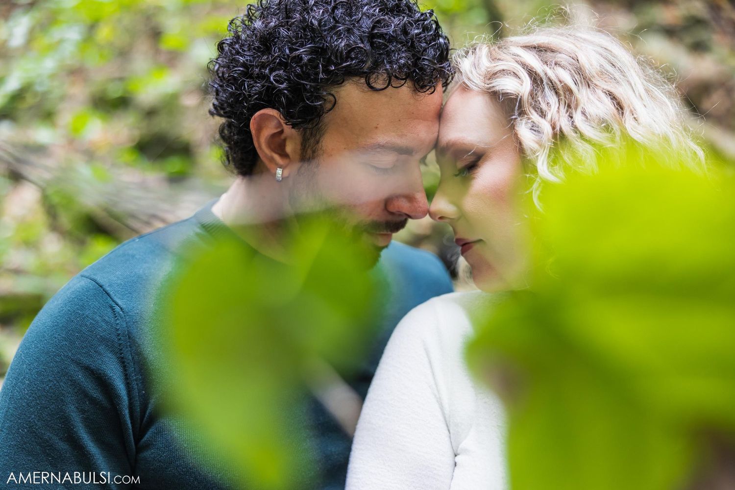 An intimate close-up moment between a couple framed by green foliage.