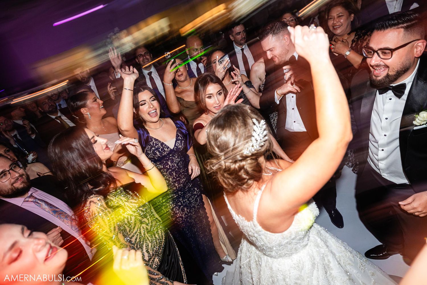 Wedding celebration with guests dancing and raising hands under dramatic lighting effects.