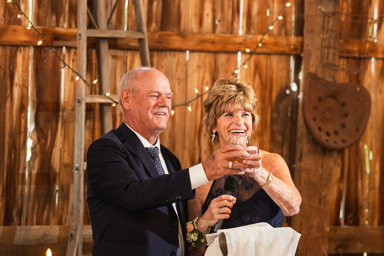 Wedding guests enjoying drinks and laughter during reception celebrations in a rustic barn setting.