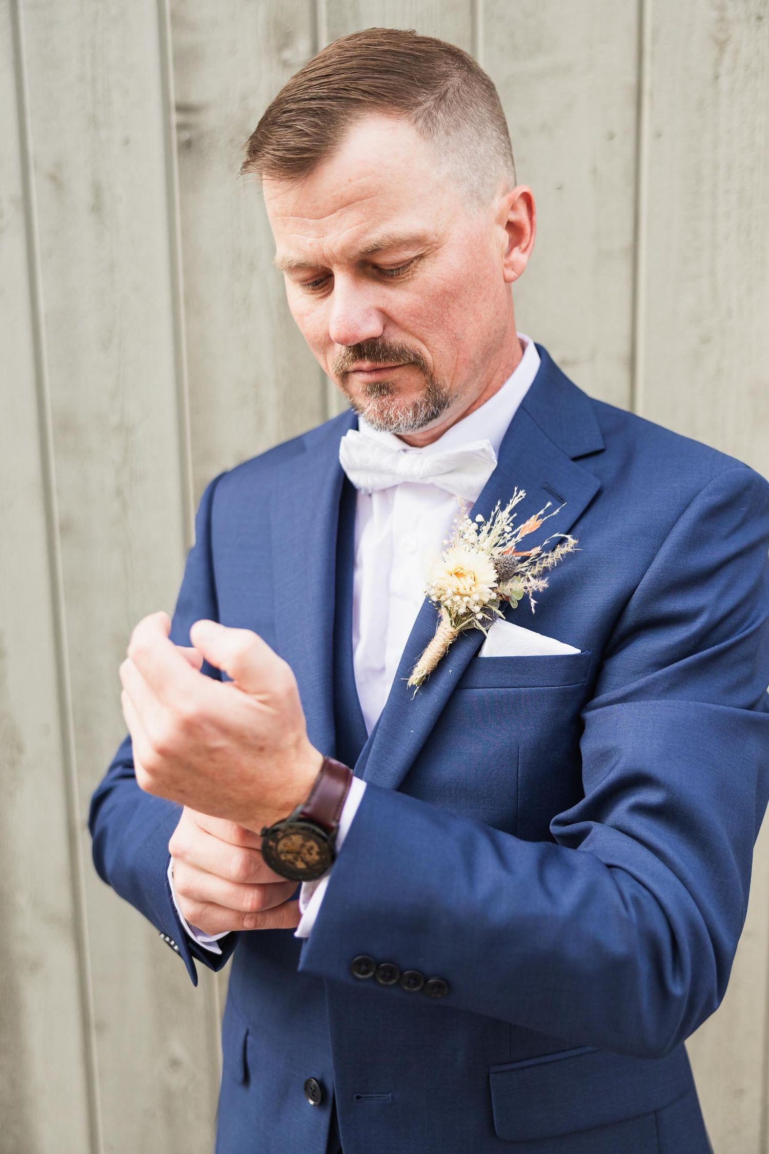 Groom in navy suit adjusts cufflinks while wearing dried floral boutonniere.