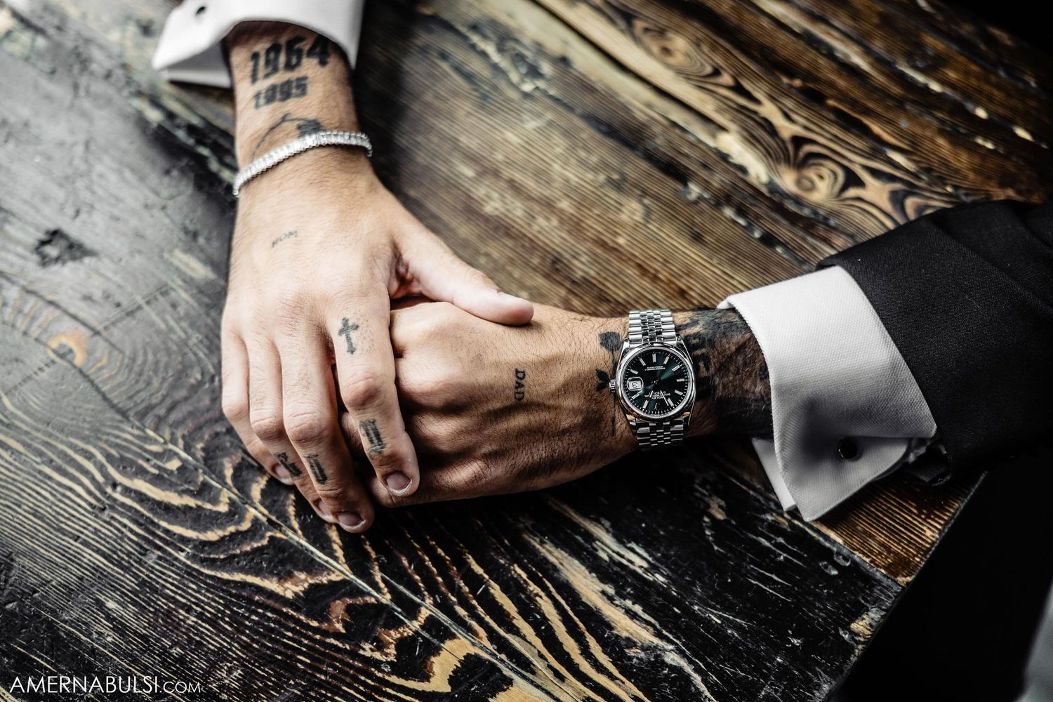 Close-up of hands wearing a luxury watch and ring on weathered wooden surface.
