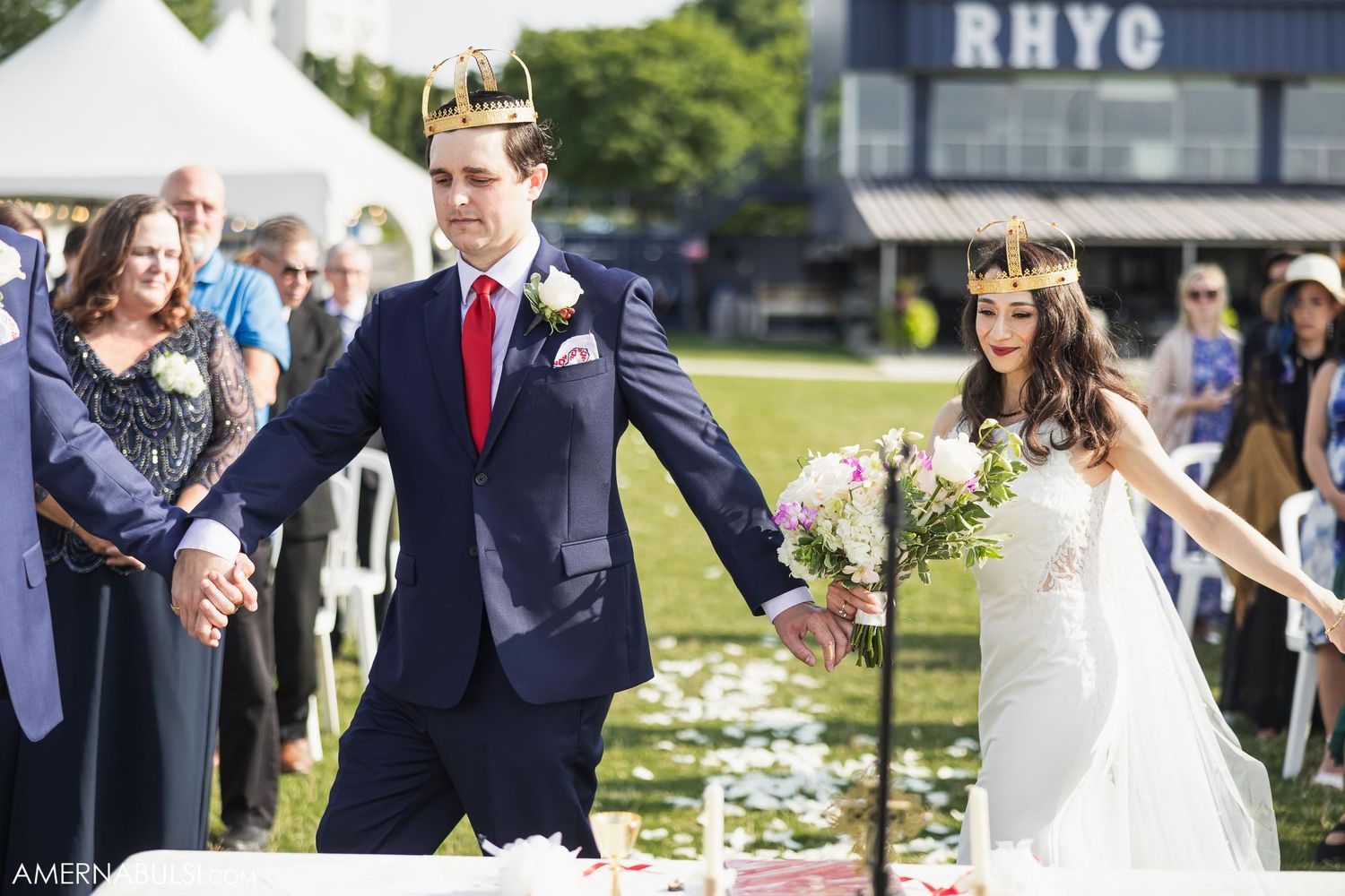 Joyful wedding celebration on grass lawn with RHYC building visible in background.