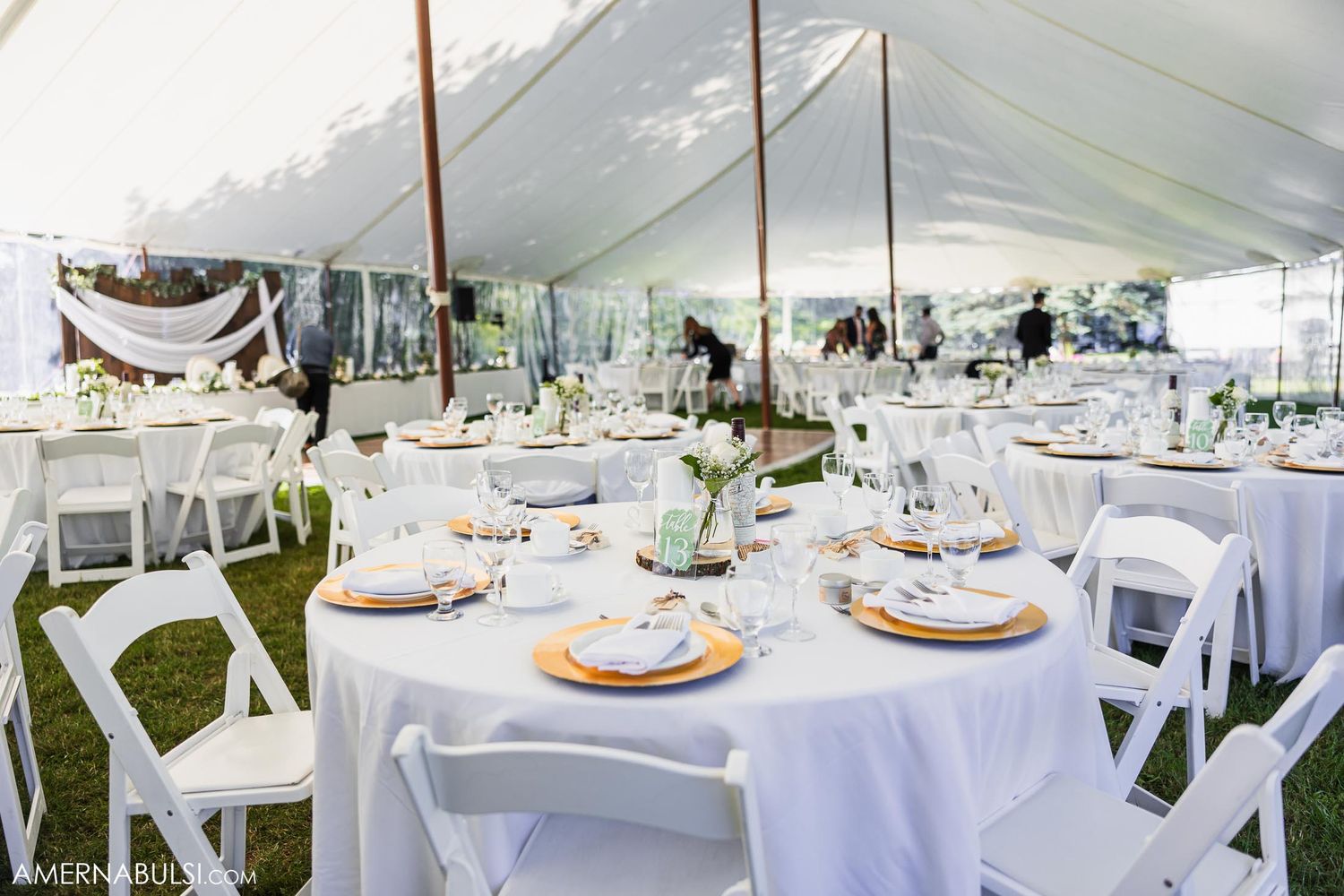 Elegant wedding reception setup with white tables and chairs under tent canopy.