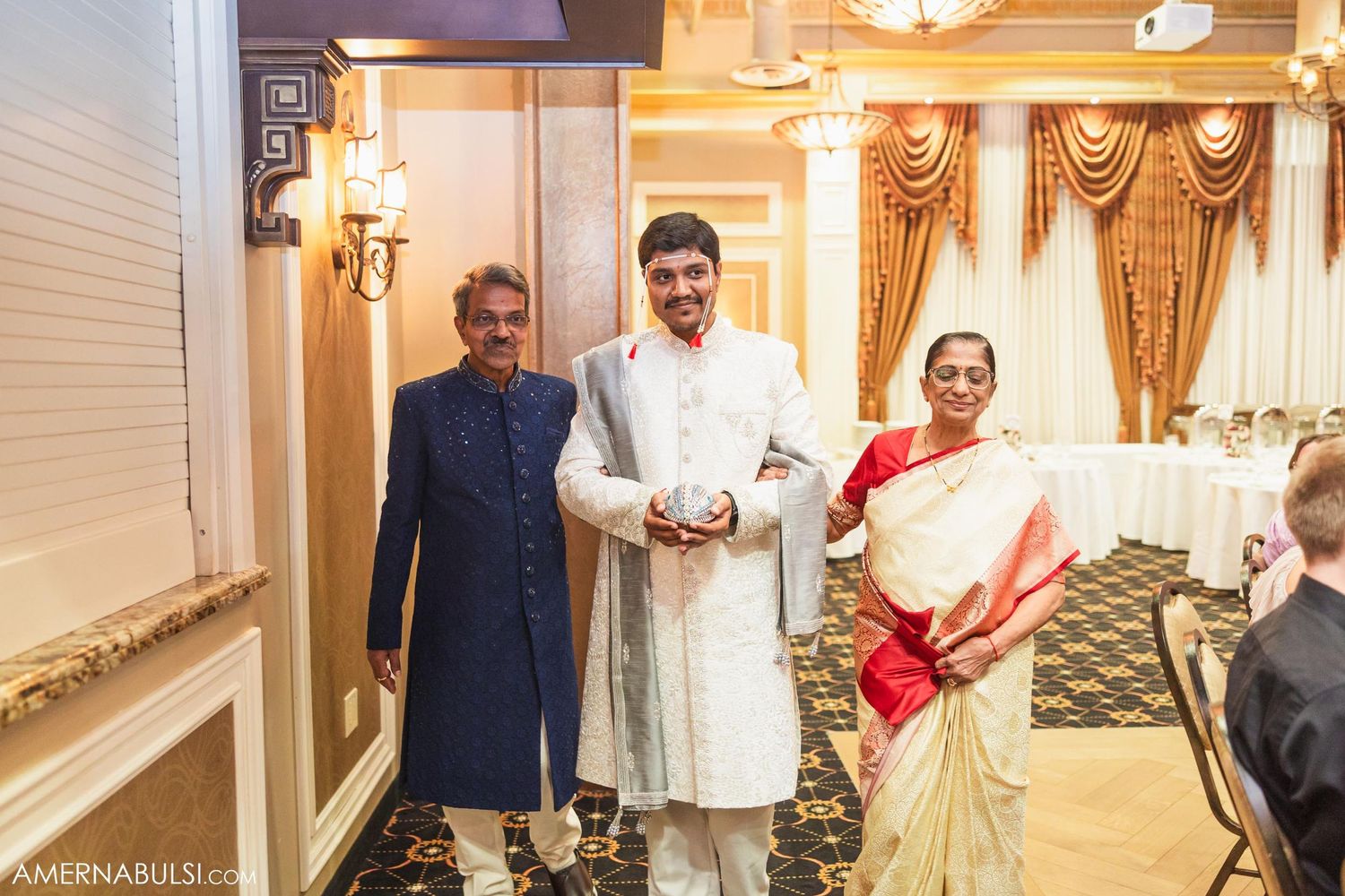 Family members in traditional Indian attire pose in an elegantly decorated hallway during a wedding celebration.