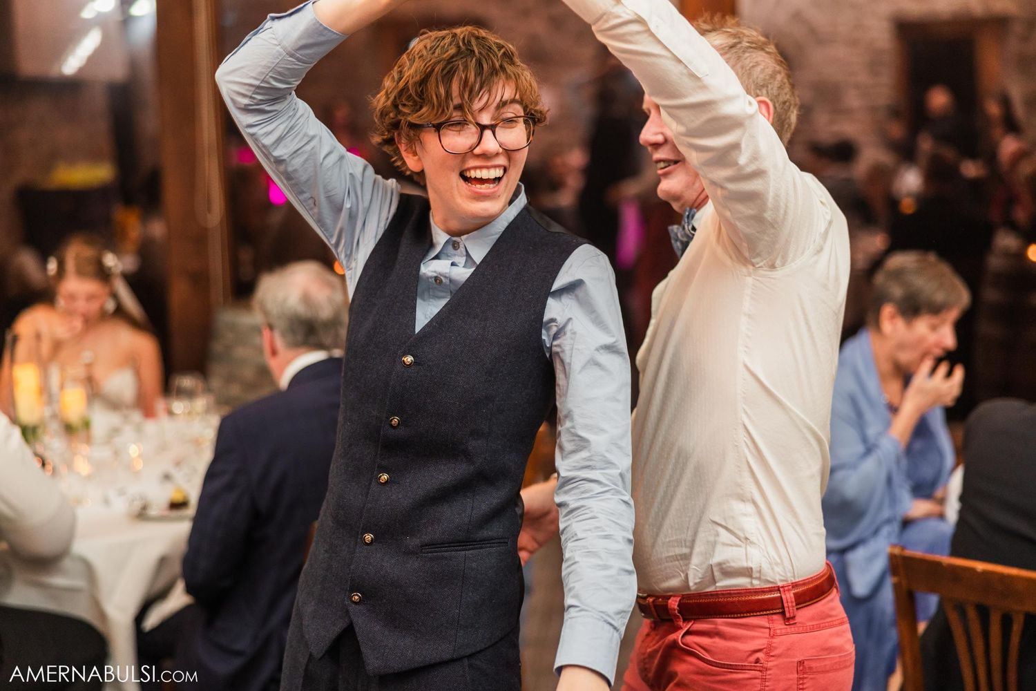 Celebratory dance moves between two guests at wedding reception in stone-walled venue.