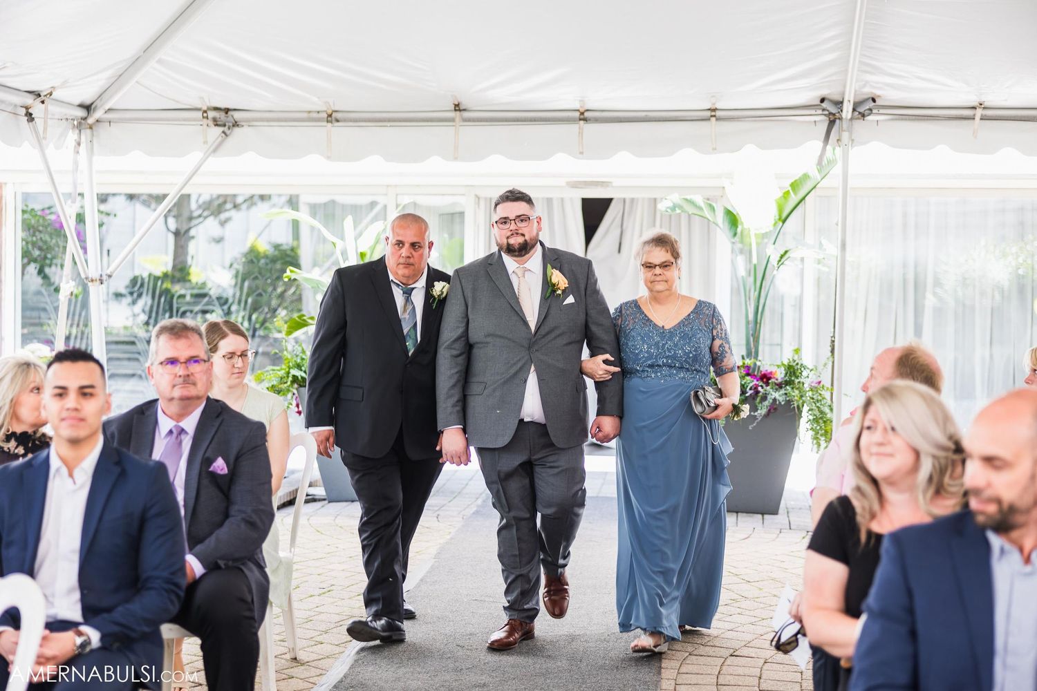 Wedding ceremony processional under a white tent with guests watching.