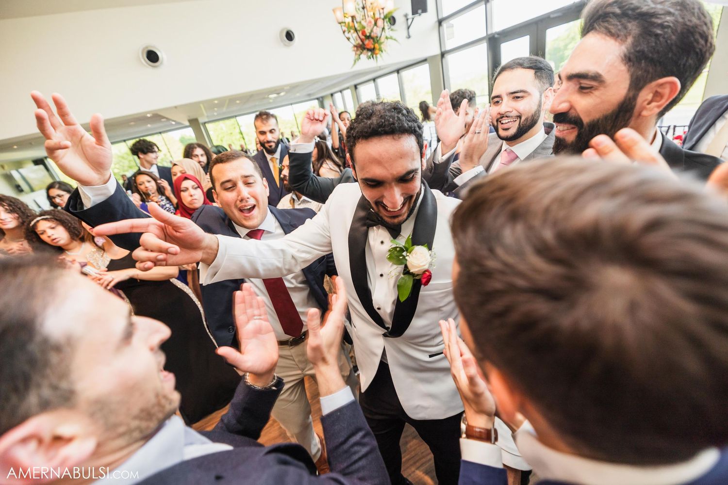 Energetic crowd of wedding guests surrounding and celebrating with excitement at indoor reception.