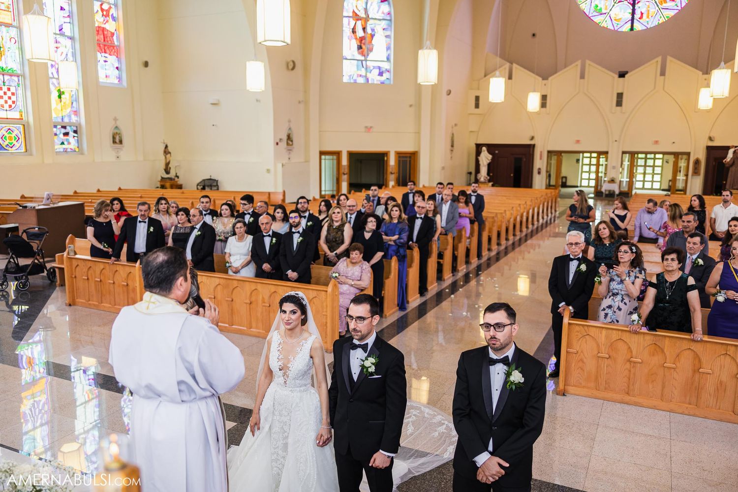 Wide view of wedding ceremony in church with guests seated in wooden pews.