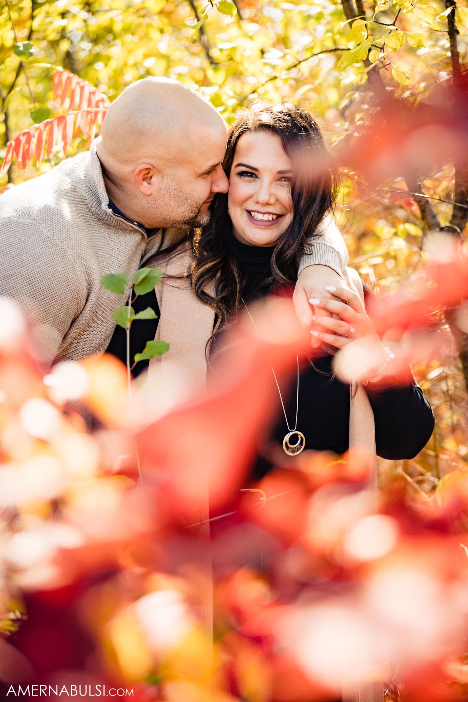 Intimate autumn portrait with red and yellow foliage framing the romantic moment.