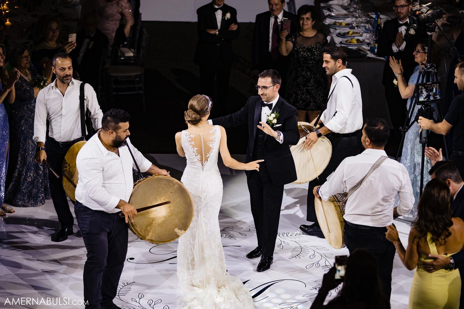 Aerial view of wedding celebration with musicians playing drums while couple dances on white floor.