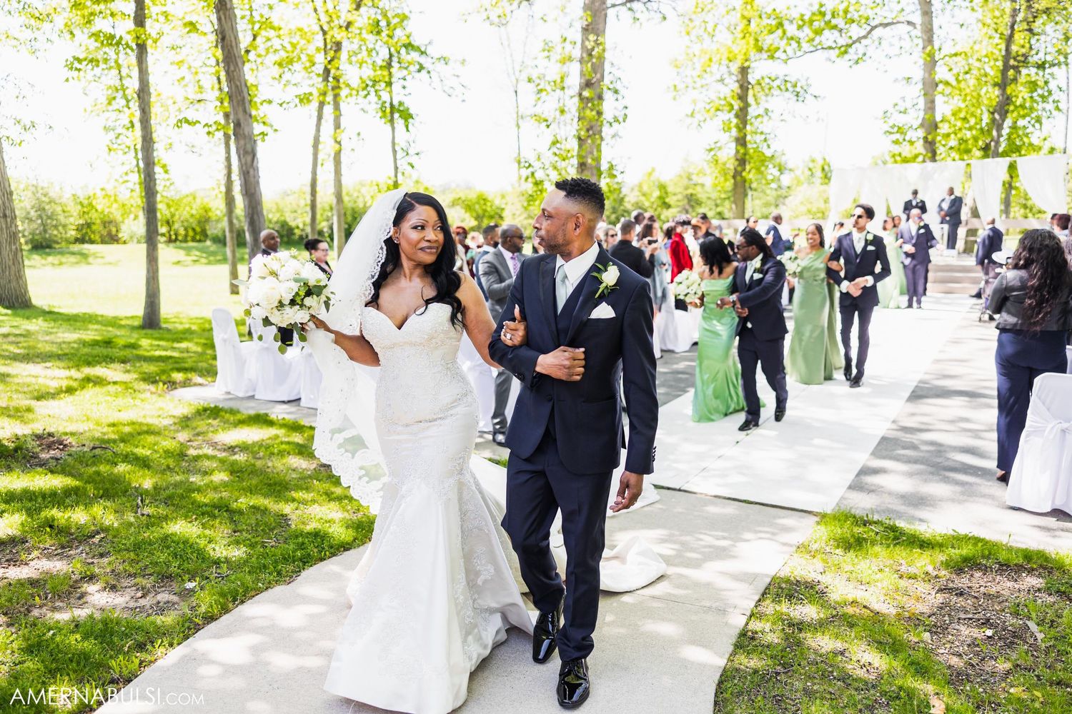 Happy newlyweds walk hand in hand along pathway after outdoor wedding ceremony.