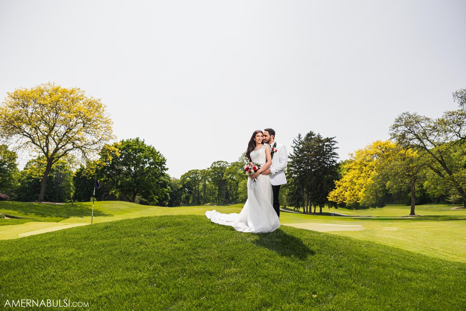 Wedding couple embracing on hilltop surrounded by manicured golf course landscape.