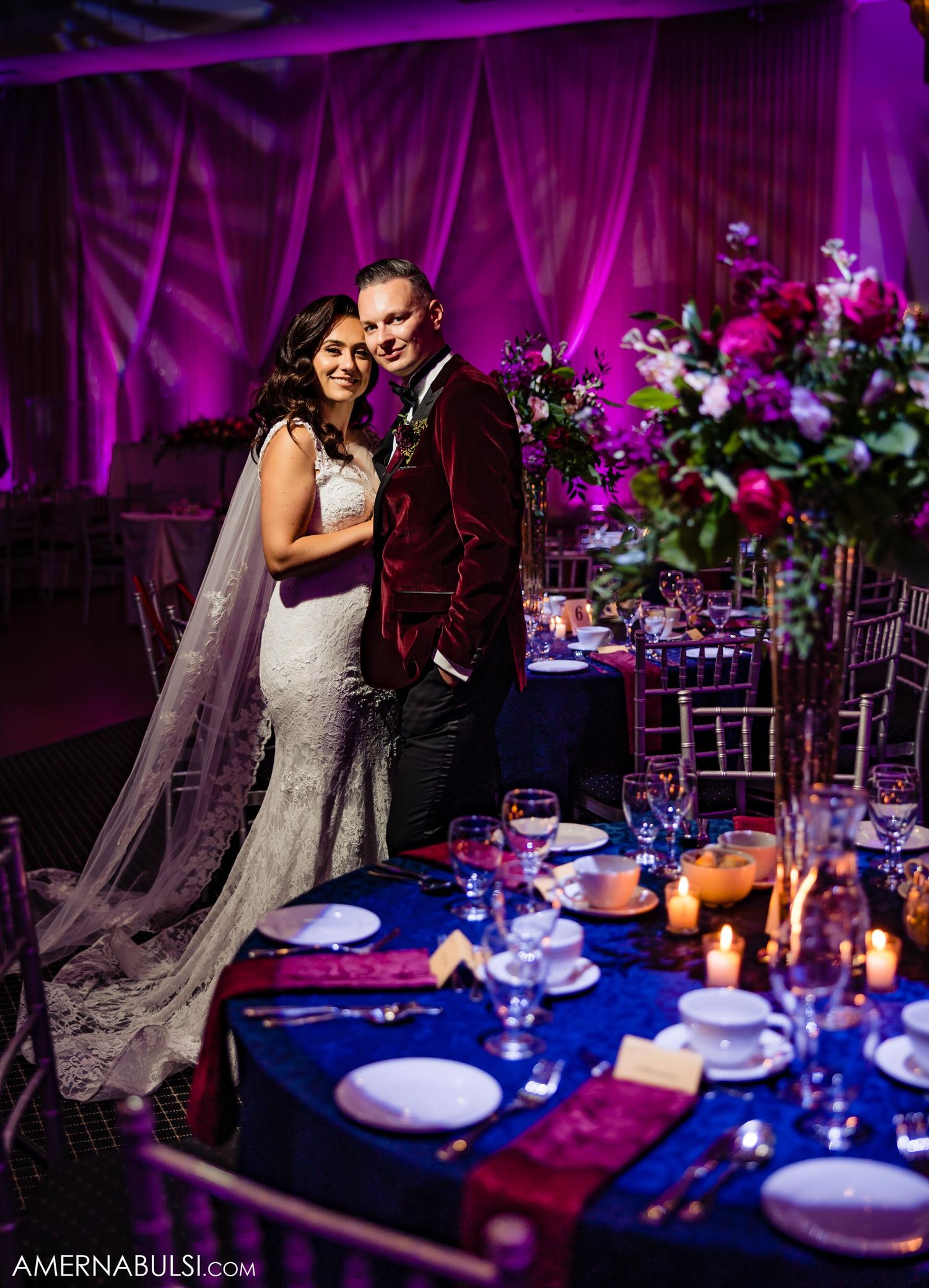 Romantic reception moment with velvet burgundy details and elegant table settings in purple lighting.