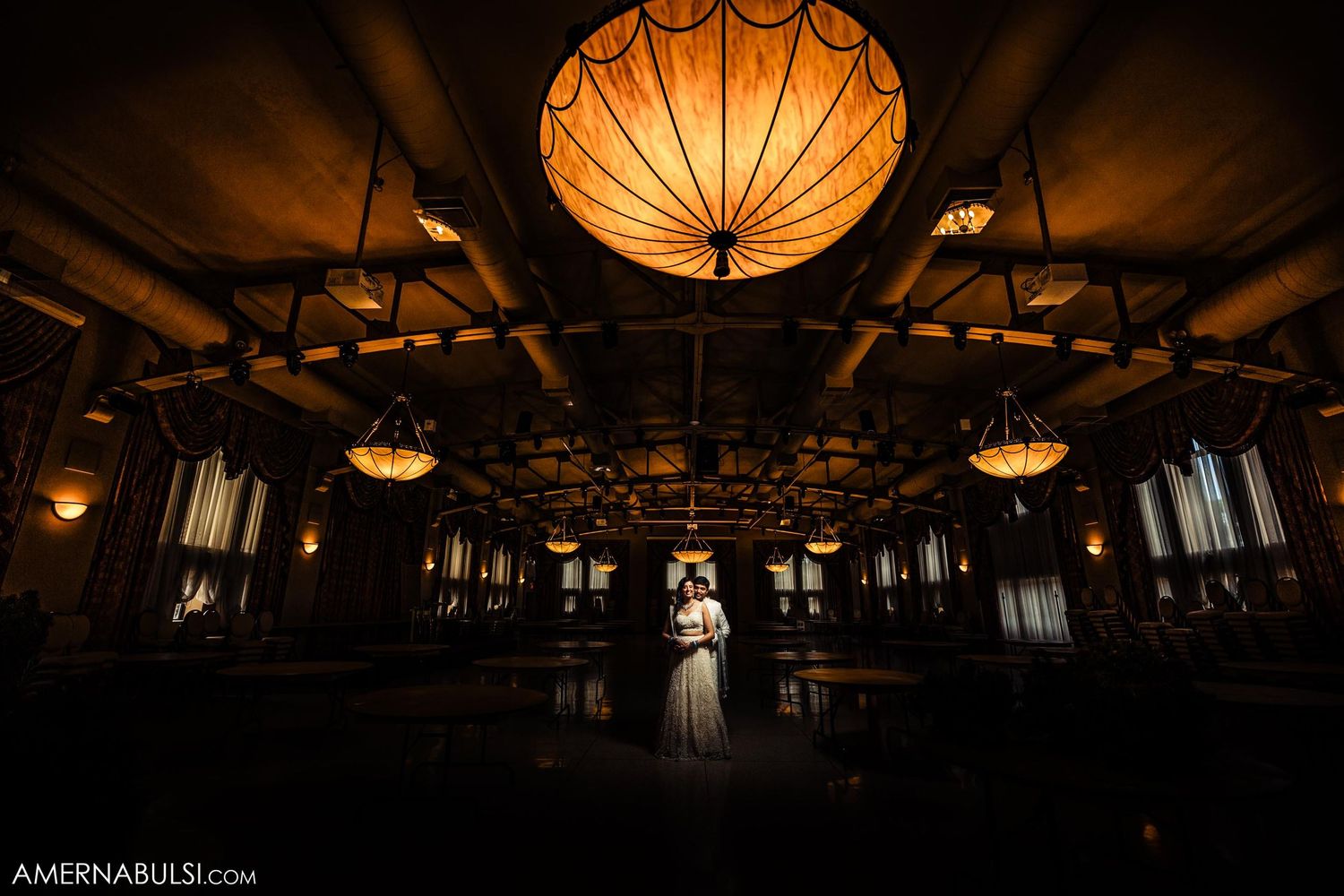 A silhouetted couple stands under dramatic orange lantern lighting in an elegant ballroom.