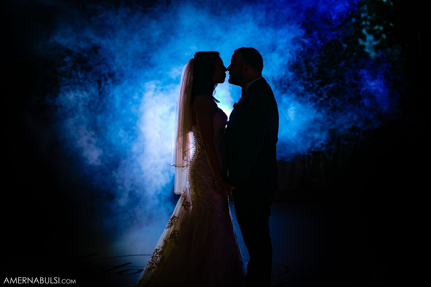 Dramatic silhouettes of a couple against deep blue atmospheric lighting during their wedding celebration.