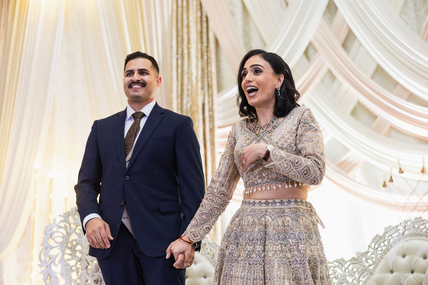Couples celebrating at an elegant wedding reception with ornate white drapes and crystal chandeliers in the background.