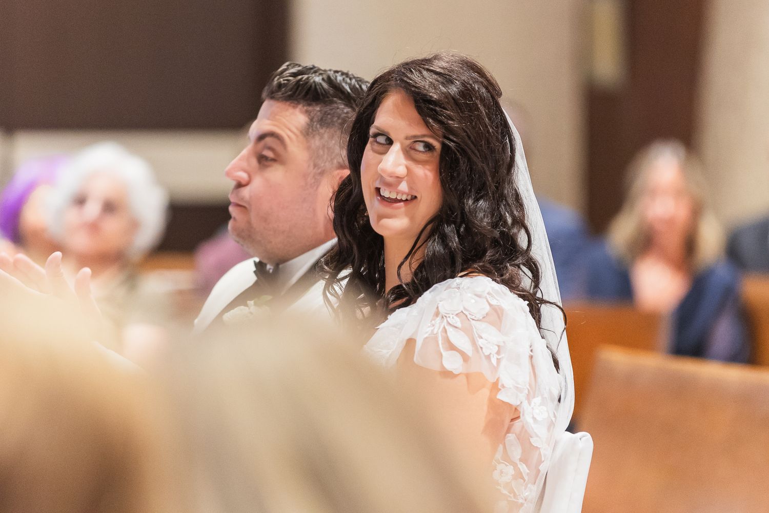 Smiling bride and groom sit together in church pews during their wedding ceremony.