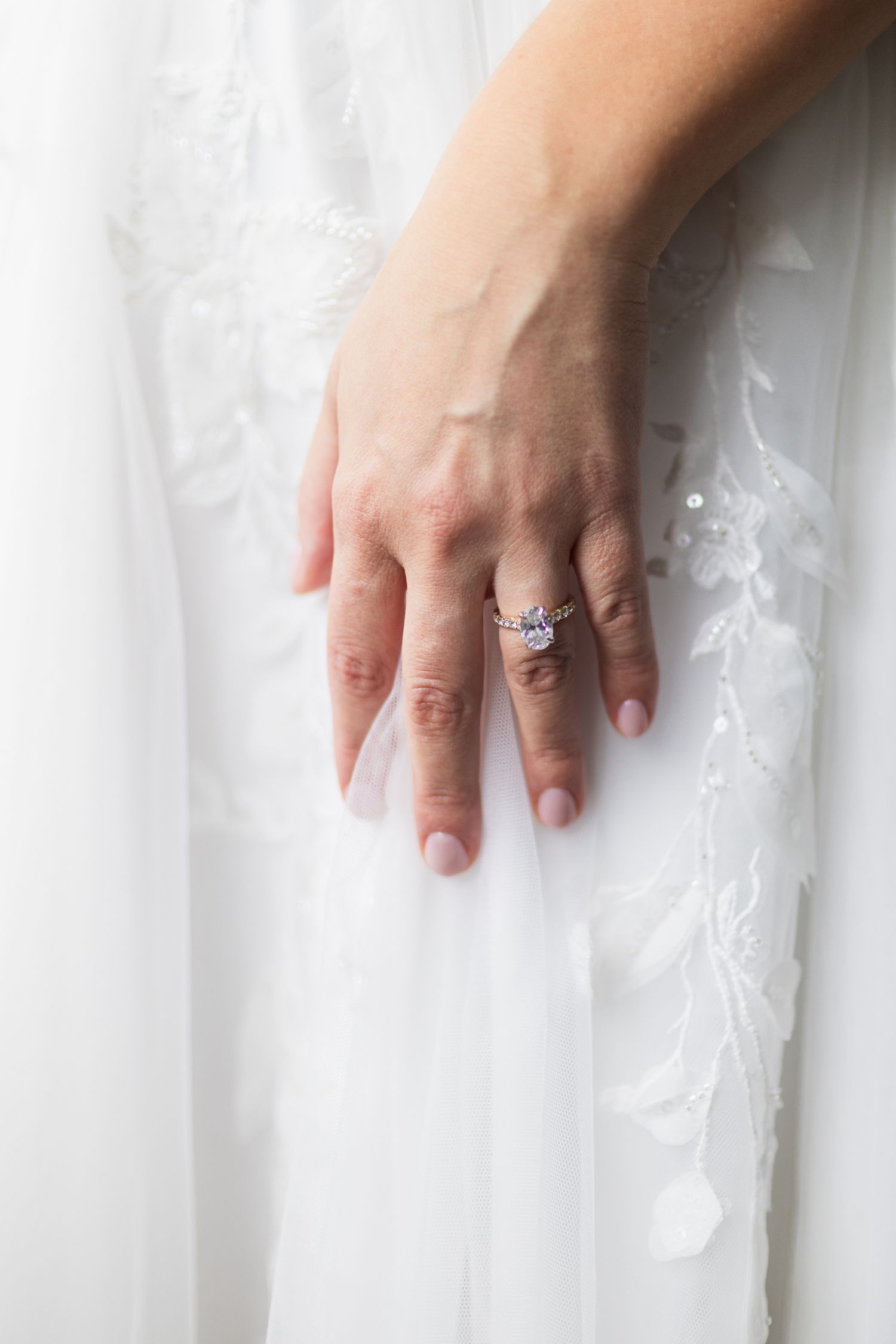 Close-up of a bride's hand displaying a stunning diamond engagement ring against her white lace wedding gown.