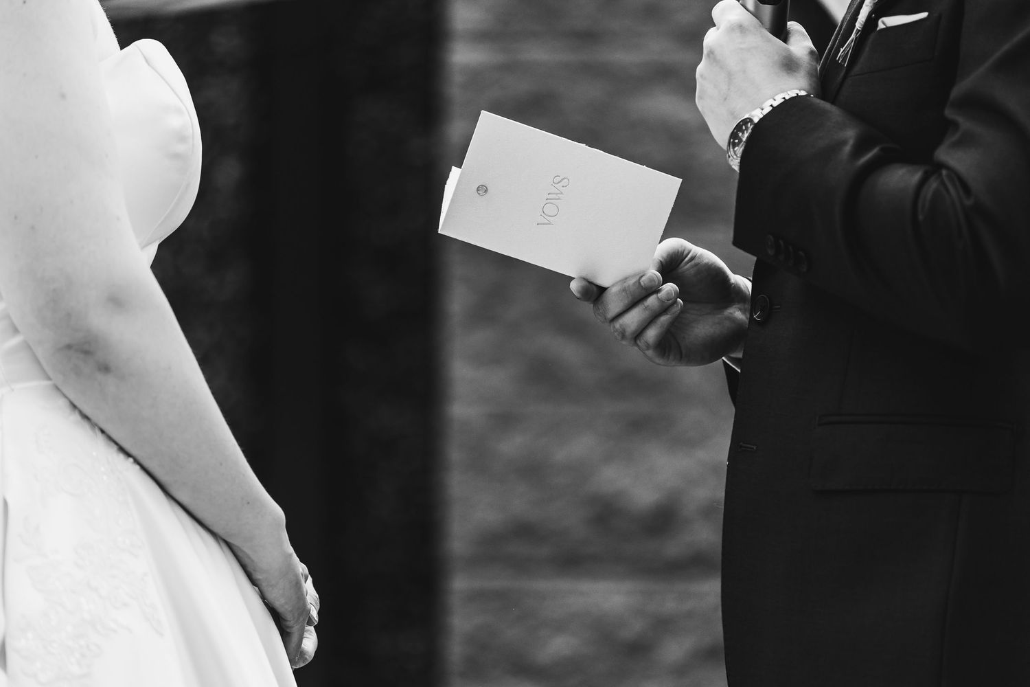 Groom reads wedding vows from a card during an outdoor ceremony in black and white photography.