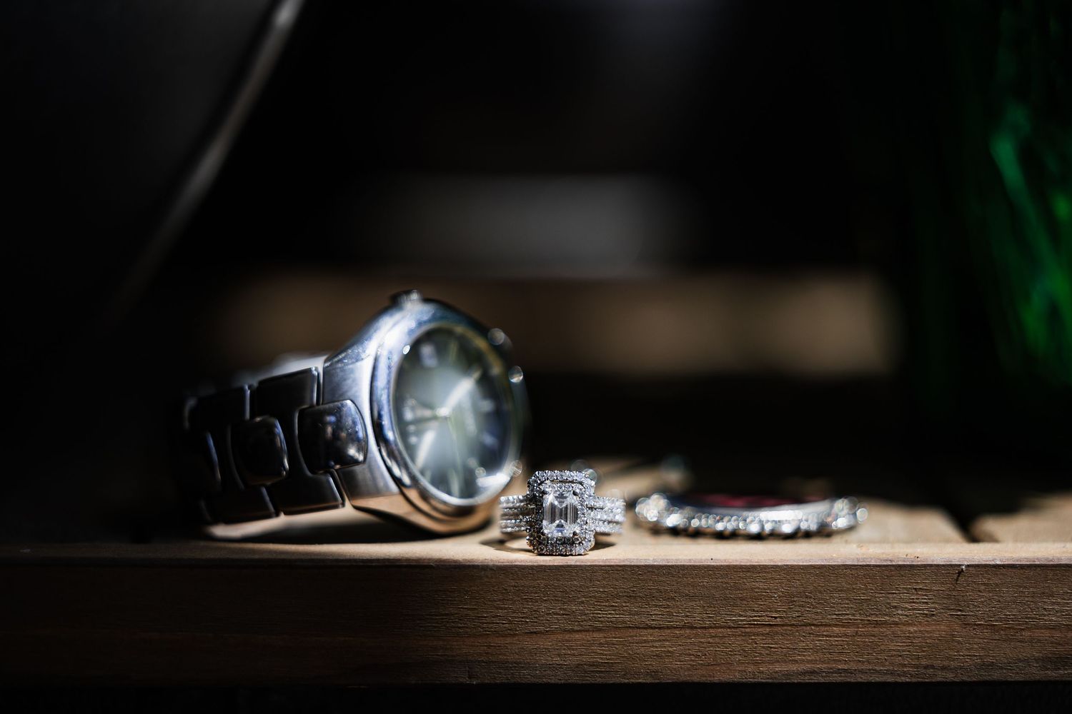 Elegant men's watch with diamond wedding rings and bracelet displayed on wooden surface in moody lighting.