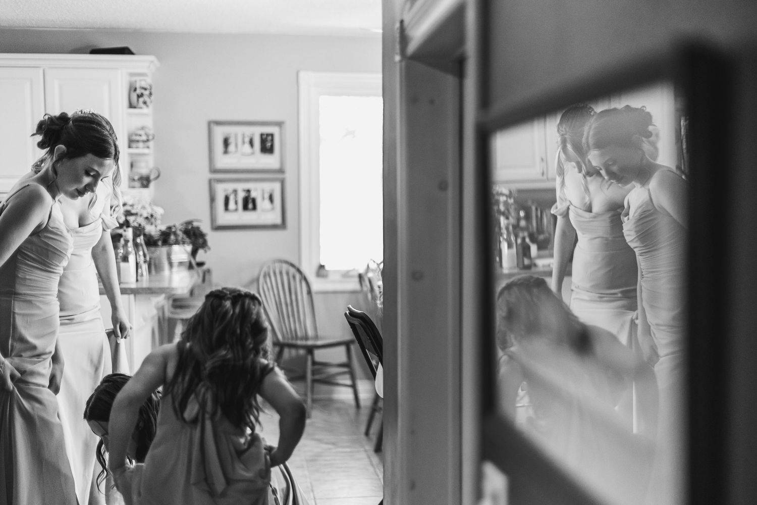 Black and white photo of women getting ready for a wedding, reflected in a mirror during bridal preparations.