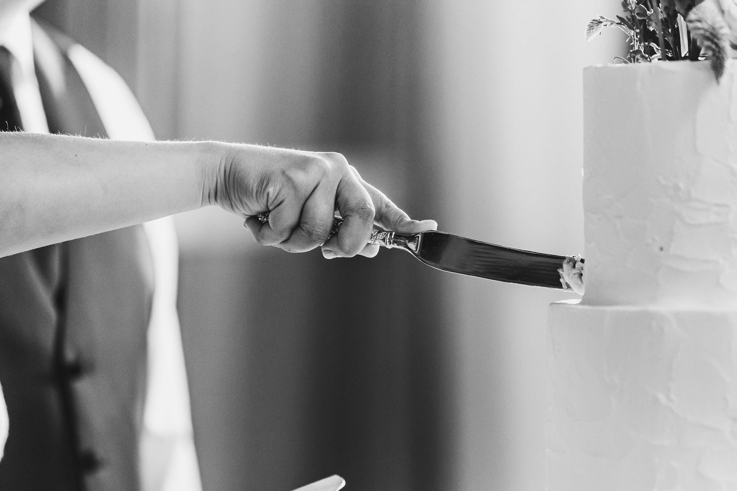 Black and white photo of a bride cutting a white wedding cake with a knife.