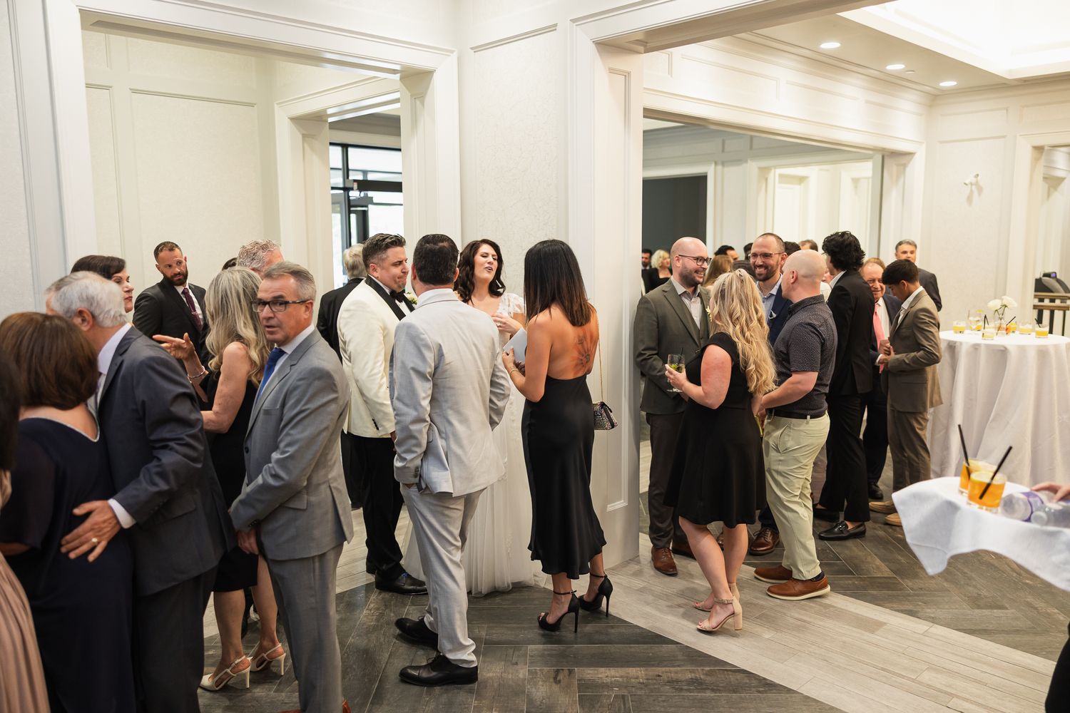 Elegantly dressed wedding guests mingle and socialize in a bright reception hall during cocktail hour.