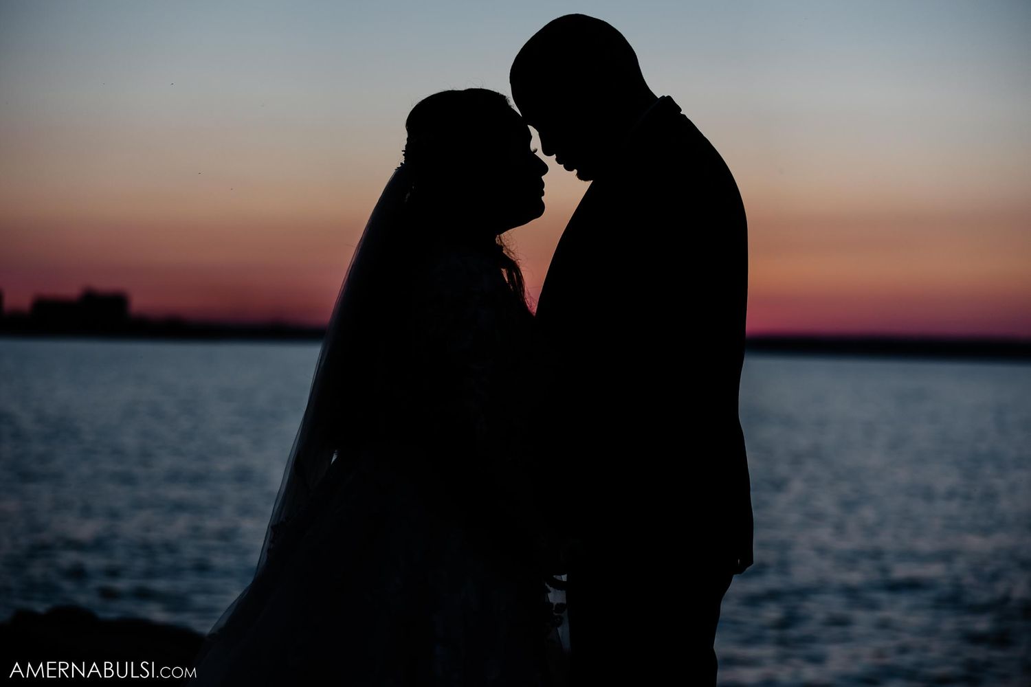 Silhouetted couple embracing against sunset waterfront backdrop.